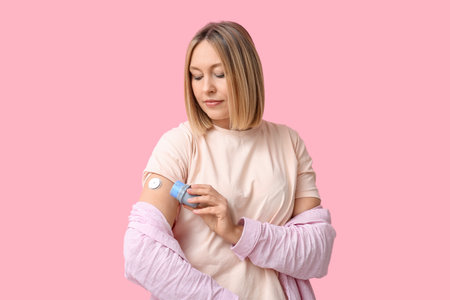 Woman with glucose sensor for measuring blood sugar level and applicator on pink background. Diabetes conceptの写真素材