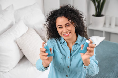 Smiling young African-American woman with asthma inhalers in bedroom