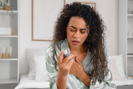 Young African-American woman with inhaler having asthma attack in bedroom