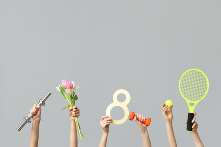 Female hands with paper figure 8, sports equipment and tulips for International Women's Day on gray backgroundの写真素材