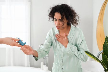 Young African-American woman receiving asthma inhaler in bathroom