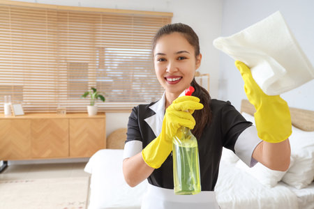 Young Asian chambermaid with detergent and rag in bedroomの写真素材