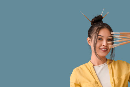 Female Asian artist with paint brushes on blue background, closeupの写真素材