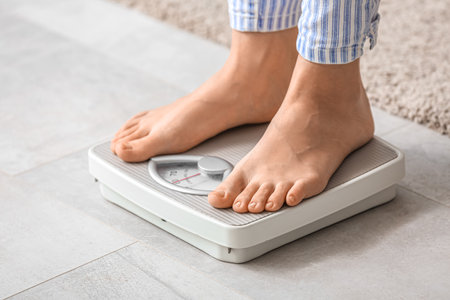 Young woman standing on scales at home. Weight loss conceptの写真素材