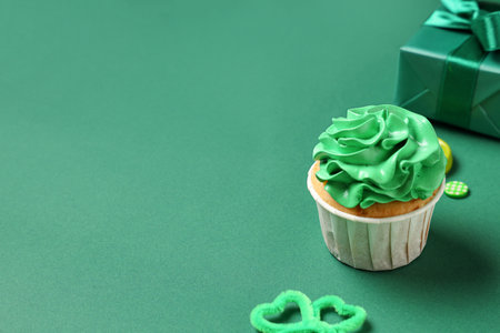 Tasty cupcake with gift box and decor for St. Patrick's Day on green backgroundの写真素材