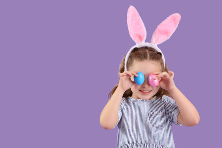 Cute little girl in bunny ears with Easter eggs on purple background