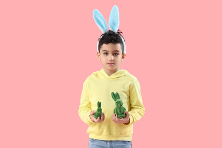 Cute little boy in bunny ears with toys rabbit on pink background. Easter celebration
