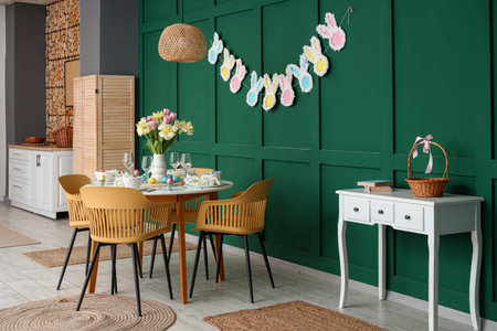 Stylish interior of festive decorated dining room with Easter table setting, vase of flowers and...