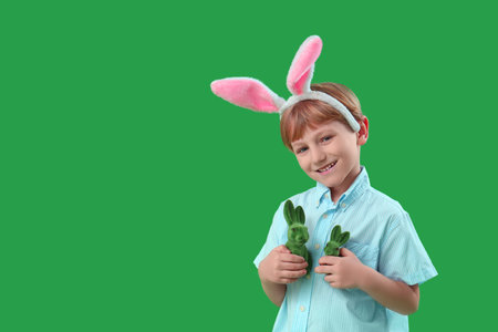 Cute little boy in bunny ears with toys rabbit on green background. Easter celebration
