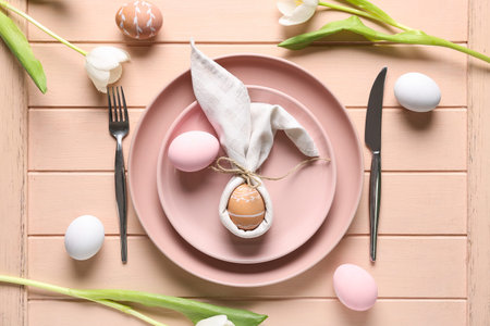Table setting with Easter eggs and beautiful tulips on pink wooden background