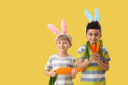 Cute little boys in bunny ears with toys carrots on yellow background. Easter celebration