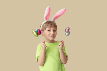 Cute little boy in bunny ears with Easter eggs on beige background