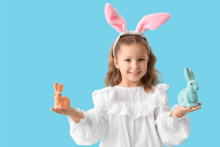 Cute little girl in bunny ears with toys rabbit on blue background. Easter celebration