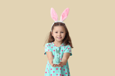Cute little girl in bunny ears with toy rabbit on beige background. Easter celebrationの写真素材