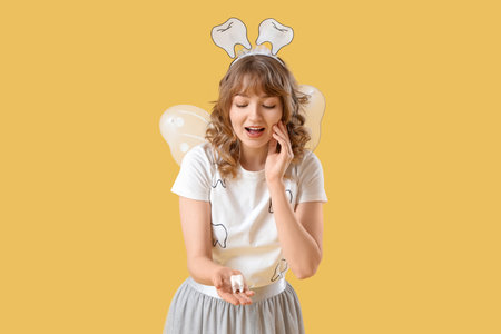 Surprised Tooth Fairy with plastic figure on yellow backgroundの写真素材