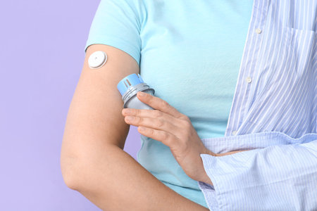 Woman with glucose sensor for measuring blood sugar level and applicator on lilac background,...