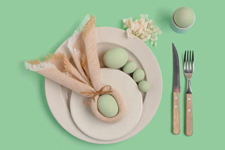Table setting with Easter eggs and beautiful flowers on green background
