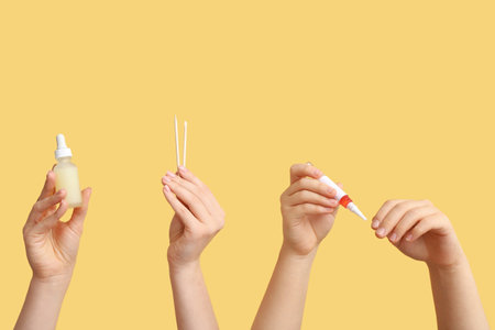 Female hands holding bottle and pen of cuticle oil with orange sticks on yellow backgroundの写真素材