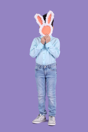 Cute little boy with paper bunny figure on purple background. Easter celebration