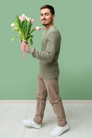 Young man with bouquet of beautiful tulips near green wall. International Women's Dayの写真素材