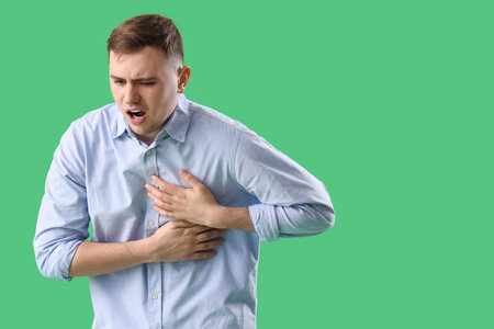 Young man suffering from chest pain on green background