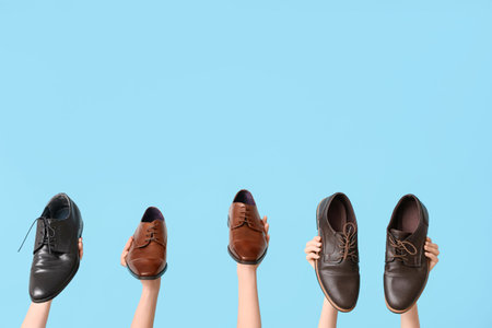 Female hands with different stylish shoes on blue background. Shoe repair concept