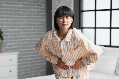 Young woman suffering from bellyache in bedroomの写真素材