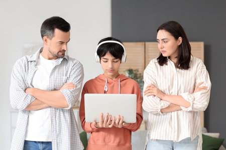 Teenage boy in headphones with laptop and his upset parents at home. Family problem conceptの写真素材