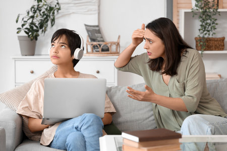 Teenage boy in headphones with laptop ignoring his mother at home. Family problem conceptの写真素材