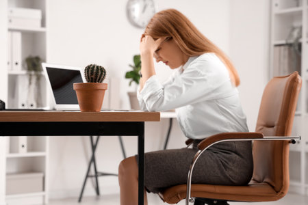 Cactus on table of mature businesswoman with hemorrhoids in officeの写真素材