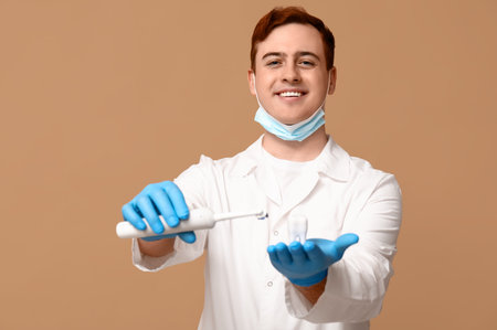 Male dentist with electric brush and tooth model on beige background. World Dentist Day
