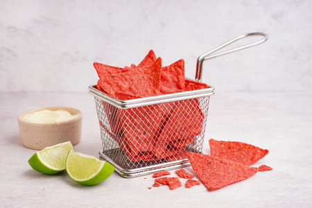 Deep fryer basket with red nachos, lime and mayonnaise on white grunge background