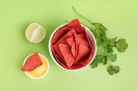 Bowl with red nachos, cheese sauce and parsley on green backgroundの写真素材