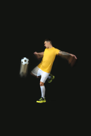 Young man playing with soccer ball in motion on black backgroundの写真素材