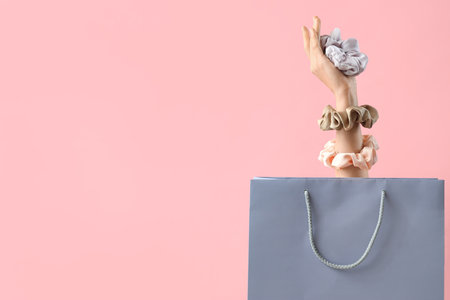 Female hand with silk scrunchies and shopping bag on pink backgroundの写真素材