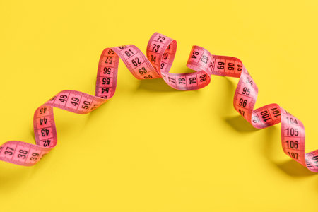 Pink measuring tape on yellow backgroundの写真素材