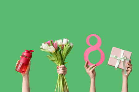 Female hands with paper figure 8, bottle of water, gift box and flowers for International Women's Day on green backgroundの写真素材