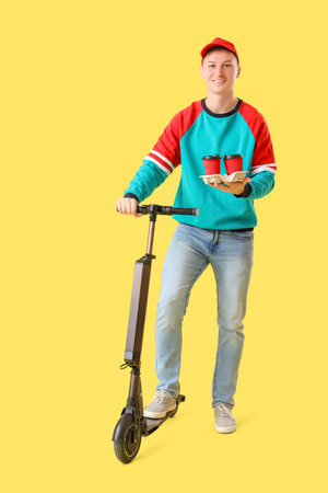 Male courier with coffee and kick scooter on yellow backgroundの写真素材