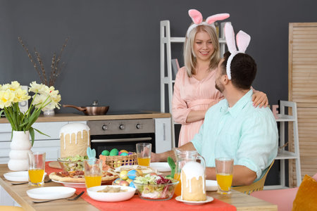 Happy couple in bunny ears having Easter dinner at home