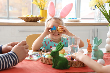 Cute little girl with painted Easter eggs at table in kitchen