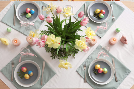 Stylish Easter table setting with flowers, cutlery, candles and painted eggs