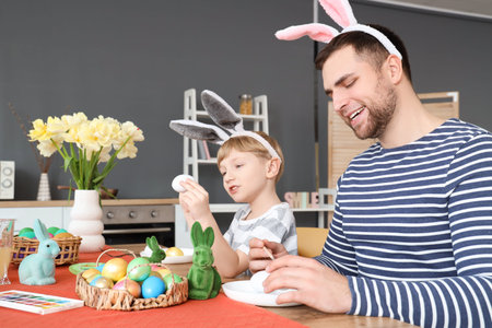 Cute little boy with his father painting Easter eggs at table in kitchenの写真素材