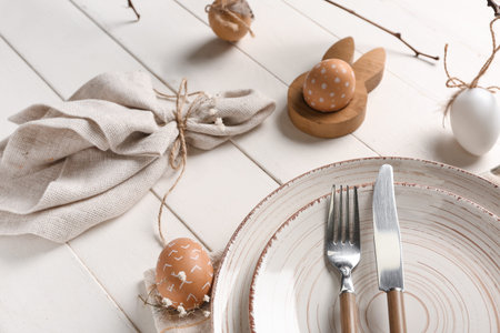 Table setting for Easter celebration with cloth and painted eggs on white wooden background