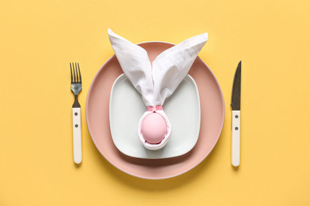 Table setting for Easter celebration with painted eggs on yellow background. Top view