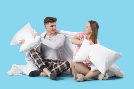 Young couple in pajamas with blanket fighting pillows on blue backgroundの写真素材