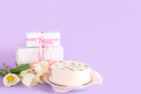 Sweet bento cake with beautiful tulips and gift boxes on lilac background. International Women's Dayの写真素材