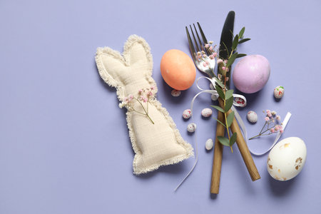 Cutlery for table setting with Easter eggs, toy bunny and gypsophila flowers on lilac backgroundの写真素材