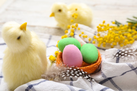 Fluffy chicks, basket with painted Easter eggs and mimosa flowers on white wooden backgroundの写真素材