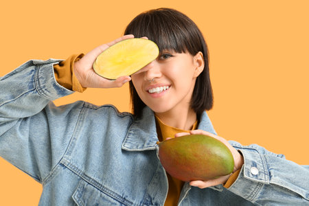 Beautiful young woman with ripe mangoes on yellow backgroundの写真素材