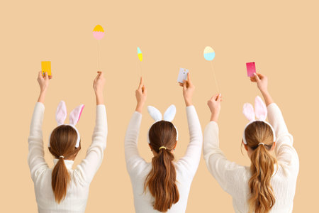 Women in bunny ears with credit cards and paper eggs on beige background, back view. Easter Saleの写真素材